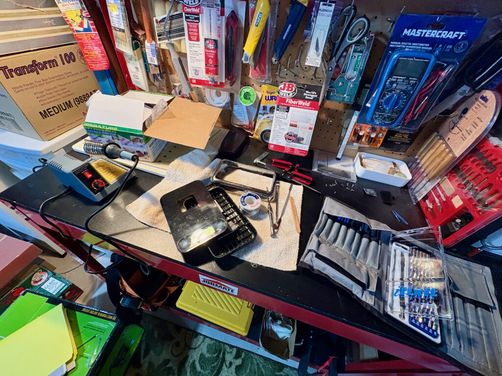 A messy work bench that has a digital scale on it, tools and soldering iron.