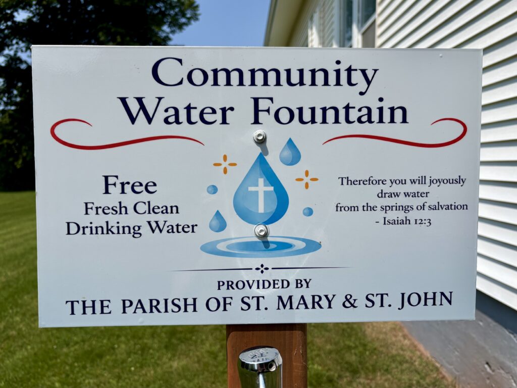 A sign that reads: Community Water Fountain. Free Fresh Clean Drinking Water. Therefore you will joyously draw water from the spring of salvation. Isaiah 12:3 Provided by the Parish of St. Mary and St. John.