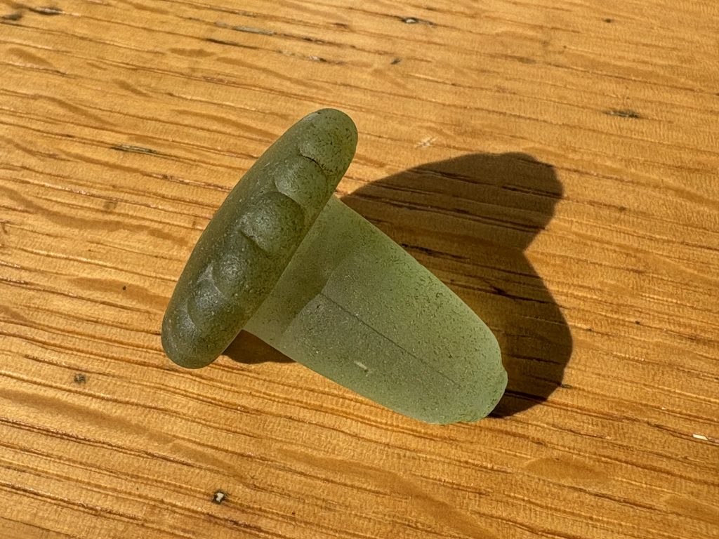 A light-green glass bottle stopper on a wooden table.
